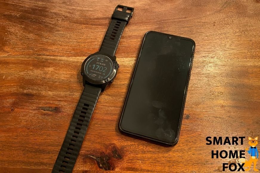 Man sieht die Garmin Fenix 6 neben einem Smartphone auf dem Tisch.